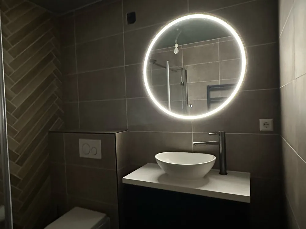 Donkere toiletruimte met verlichte ronde spiegel en waskom