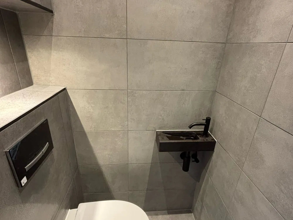 Betegelde toiletruimte met inbouwreservoir en fonteintje